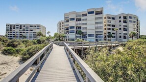 Une promenade en bois mène à un hôtel en bord de mer, doté de nombreux balcons et offrant une vue dégagée sur l’océan.