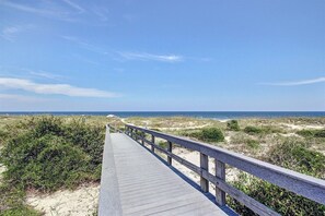 A wooden boardwalk leading to a beach with dunes and vegetation.