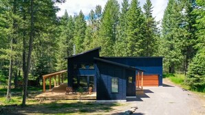 Eine moderne Hütte mit überdachter Veranda, Garage und einem Schotterweg, umgeben von dichtem Wald.