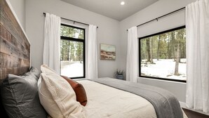 Ein Schlafzimmer mit einem großen Bett, zwei Fenstern, einem Gemälde und Blick auf einen verschneiten Wald.
