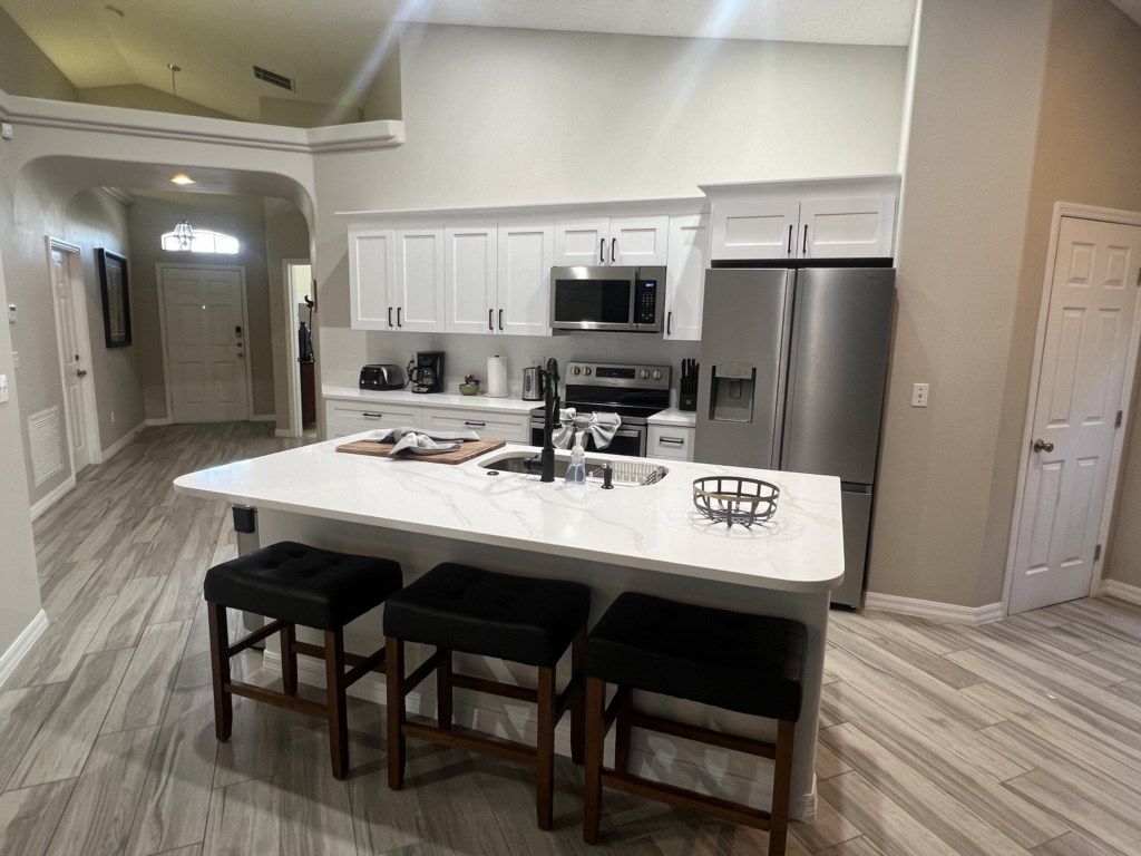 A modern kitchen with a central island, bar stools, stainless steel appliances, and white cabinetry.
