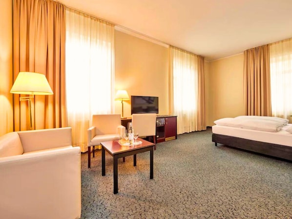 Una habitación de hotel con cama, escritorio, dos sillas, televisor y un mini bar.