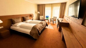 Habitación de hotel con dos camas, un escritorio, una silla, un televisor y una ventana con cortinas.