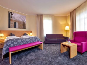 Una habitación de hotel con una cama, un sofá, una silla, una mesita y una lámpara.