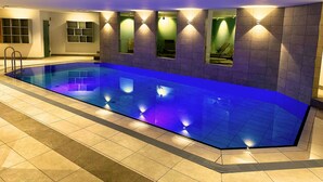 Una piscina con tonalidades azules, paredes enlosadas e iluminación empotrada.