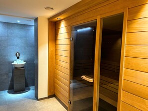Un baño moderno con pared de paneles de madera, cabina de ducha con mampara de vidrio y lavamanos sobre pedestal con lavabo de cristal.