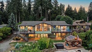 A two-story house with a covered patio, a deck, and a stone fire pit. - Lakefront Home with Hot Tub, Kayaks, Fire Pit, & Breakfast Included (Black Diamond)