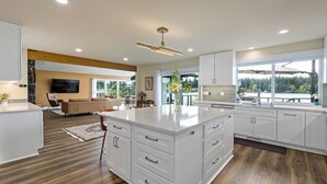 A modern kitchen with white cabinetry, a large island, and a dining area with a view of the outdoors. - Lakefront Home with Hot Tub, Kayaks, Fire Pit, & Breakfast Included (Black Diamond)