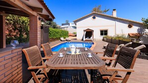 Una veranda con piscina, mobili in legno e una casa sullo sfondo.