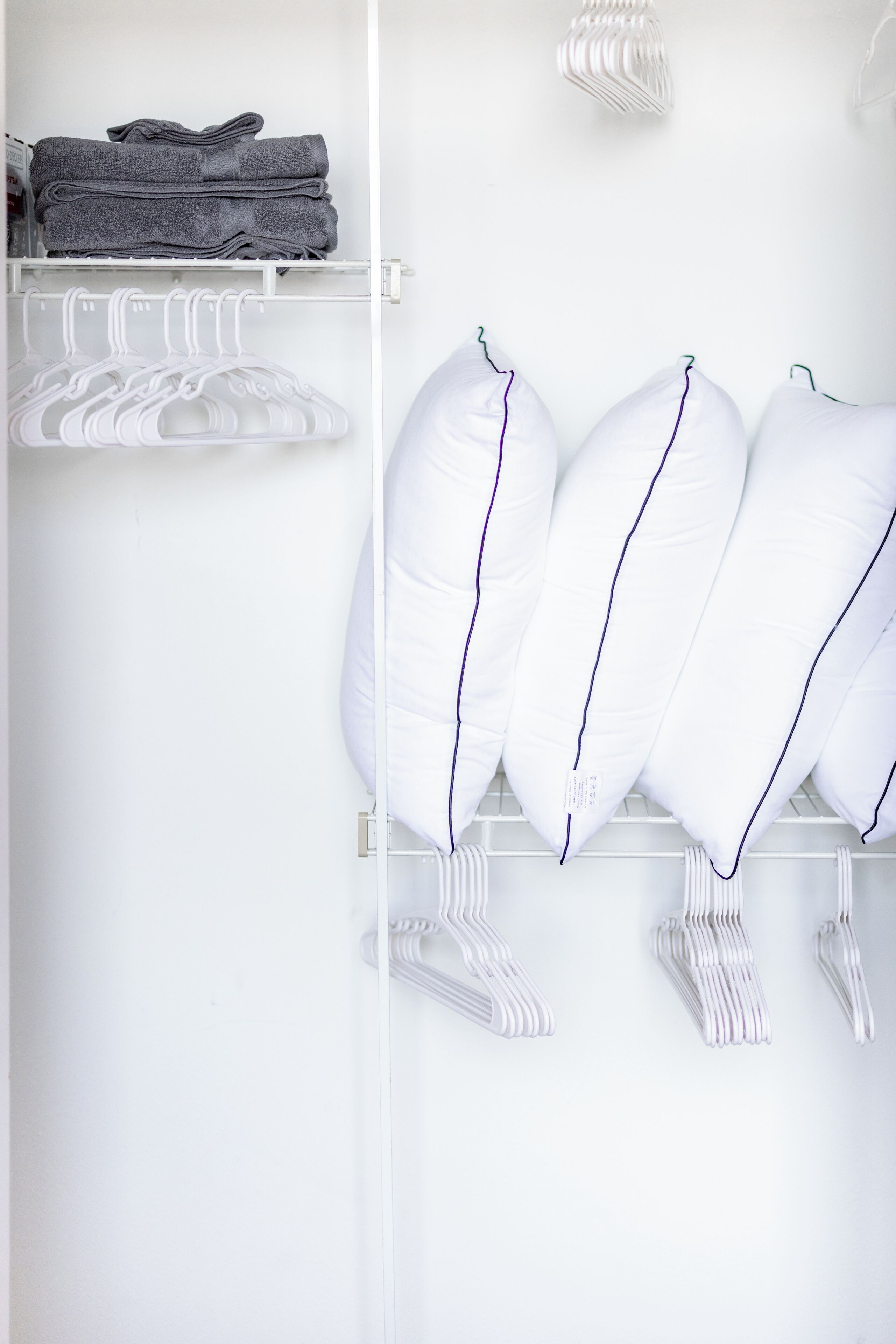 Un placard bien rangé, avec des serviettes pliées et des cintres blancs.