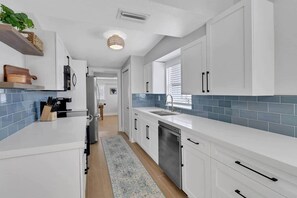 Una cucina moderna con mobili bianchi, una parete rivestita di piastrelle blu, una lavastoviglie integrata e un'isola centrale.
