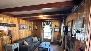 Interior acogedor de una cabaña con paredes de madera, un sofá, una mesa de centro y una chimenea.
