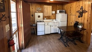 Una cocina rústica con paredes de madera, estufa a gas, un lavamanos y un refrigerador.