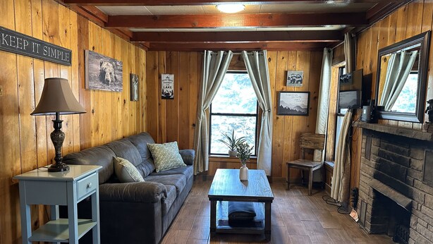 Una habitación acogedora con detalles de madera, un sofá, una mesa, una lámpara y una chimenea.