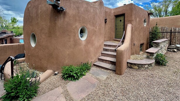 A stucco building with a green door, circular windows, and a stone staircase leading to the entrance. - Elegant casita in the middle of Santa Fe's historic Canyon Road district  (Santa Fe)