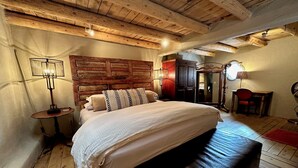 A cozy bedroom with a wooden headboard, a large bed, a small table, and a chair. - Elegant casita in the middle of Santa Fe's historic Canyon Road district  (Santa Fe)