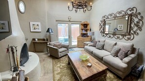A cozy living room with a wooden ceiling, a chandelier, a sofa set, a coffee table, and a fireplace. - Elegant casita in the middle of Santa Fe's historic Canyon Road district  (Santa Fe)
