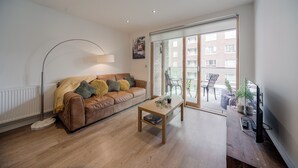 A modern living room with a leather sofa, a wooden coffee table, and a floor lamp. - Barking Bright Apartment With 2 Bedrooms (Barking)