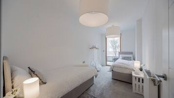 A modern bedroom with two beds, a large window, and a radiator.