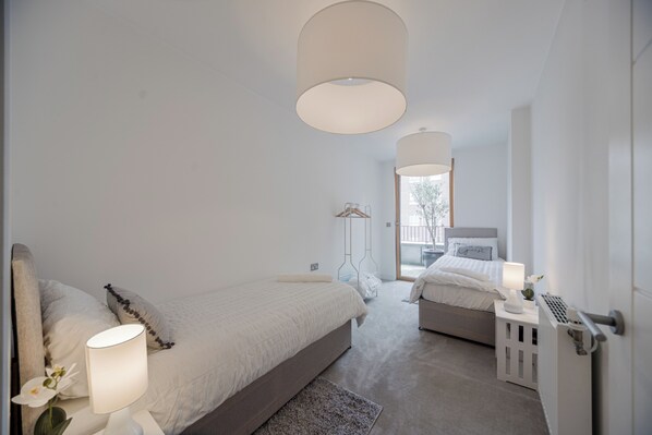 A modern bedroom with two beds, a large window, and a radiator.