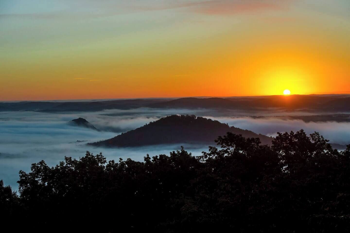 Een zonsopgang boven een bergketen met een bebost voorplan.