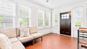 A room with a beige sofa, white brick walls, a red-tiled floor, and a dark wooden door.