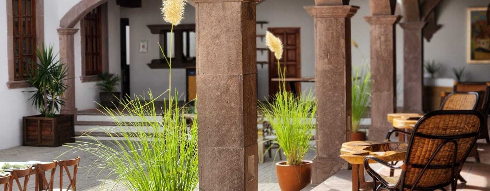 Un patio al aire libre con columnas de piedra, plantas en macetas y mobiliario de mimbre.