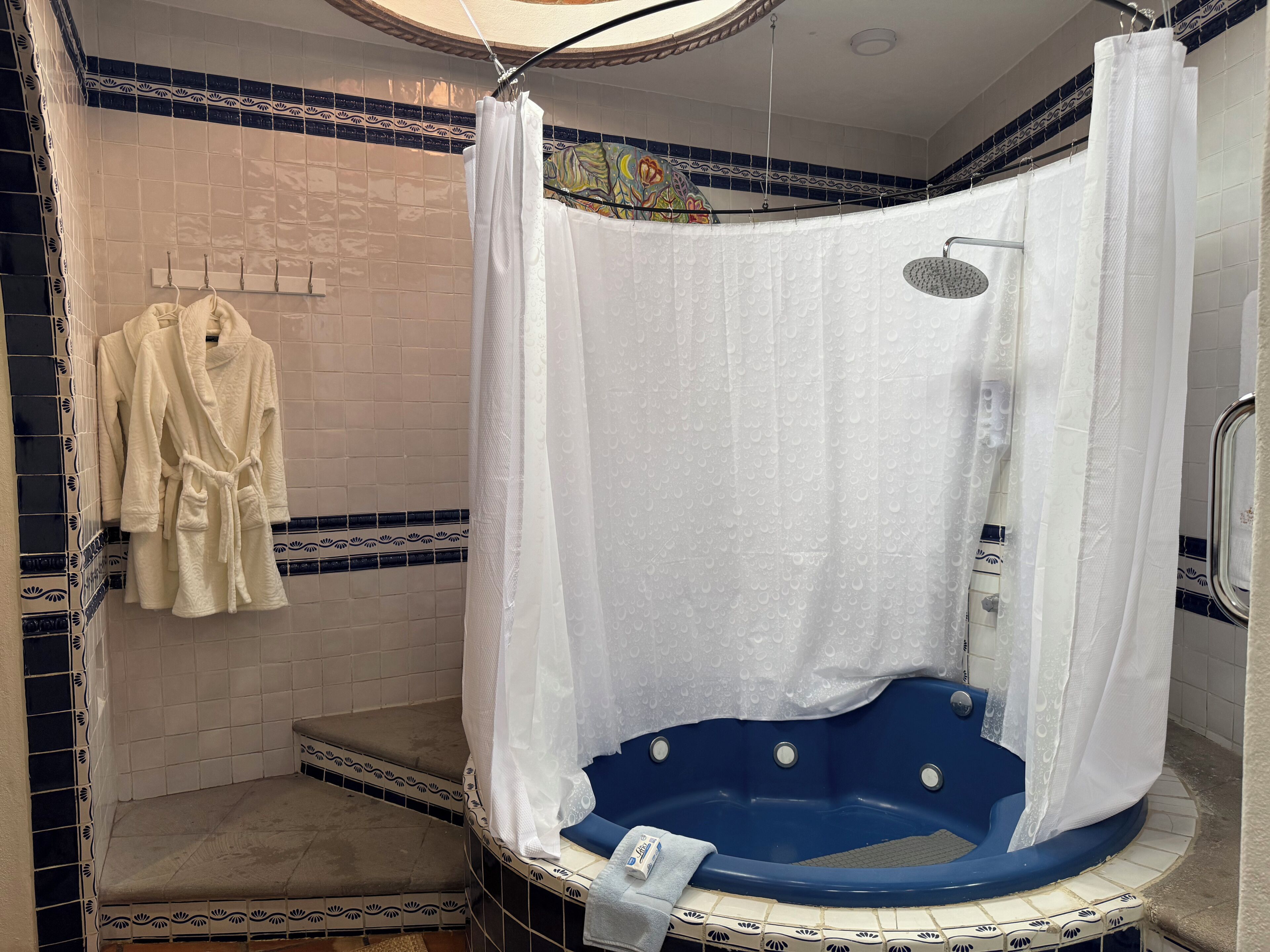 A bathroom with a blue jacuzzi tub, a shower curtain, and a towel rack with robes.