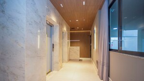 Un pasillo moderno con paredes de mármol, techo de madera y una puerta de cristal que da a una habitación.