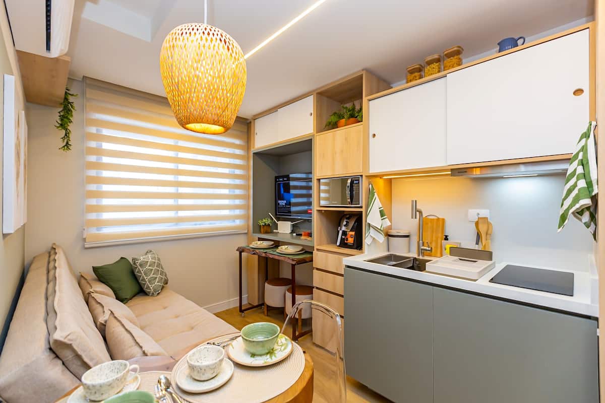 Un espace de vie compact comprenant un coin cuisine, un coin repas avec une table pour deux personnes et un canapé avec des coussins.