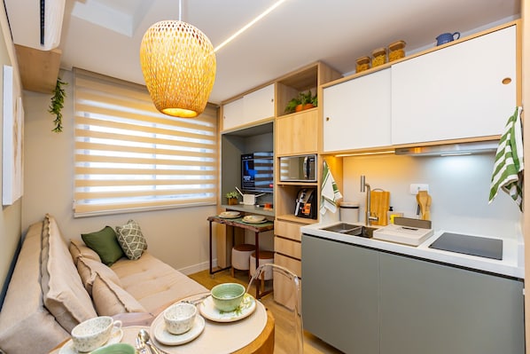 A compact living space with a kitchenette, a dining area with a table set for two, and a sofa with cushions.