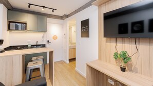 Una cocina moderna con microondas integrado, una zona de bar con taburetes, un televisor de pantalla plana montado en una pared de madera y una planta en maceta.