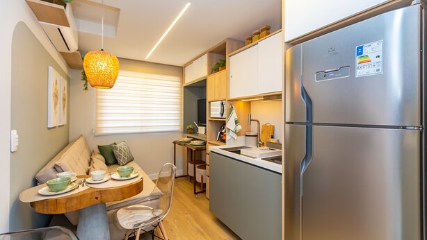 Una cocina compacta con refrigerador incorporado, una zona de comedor con mesa y sillas de madera, y una lámpara colgante.