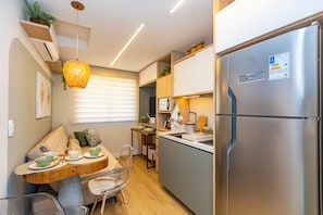 A compact kitchen with a built-in refrigerator, a dining area with a wooden table and chairs, and a hanging light fixture. - Edifício Lins 236 (Curitiba)