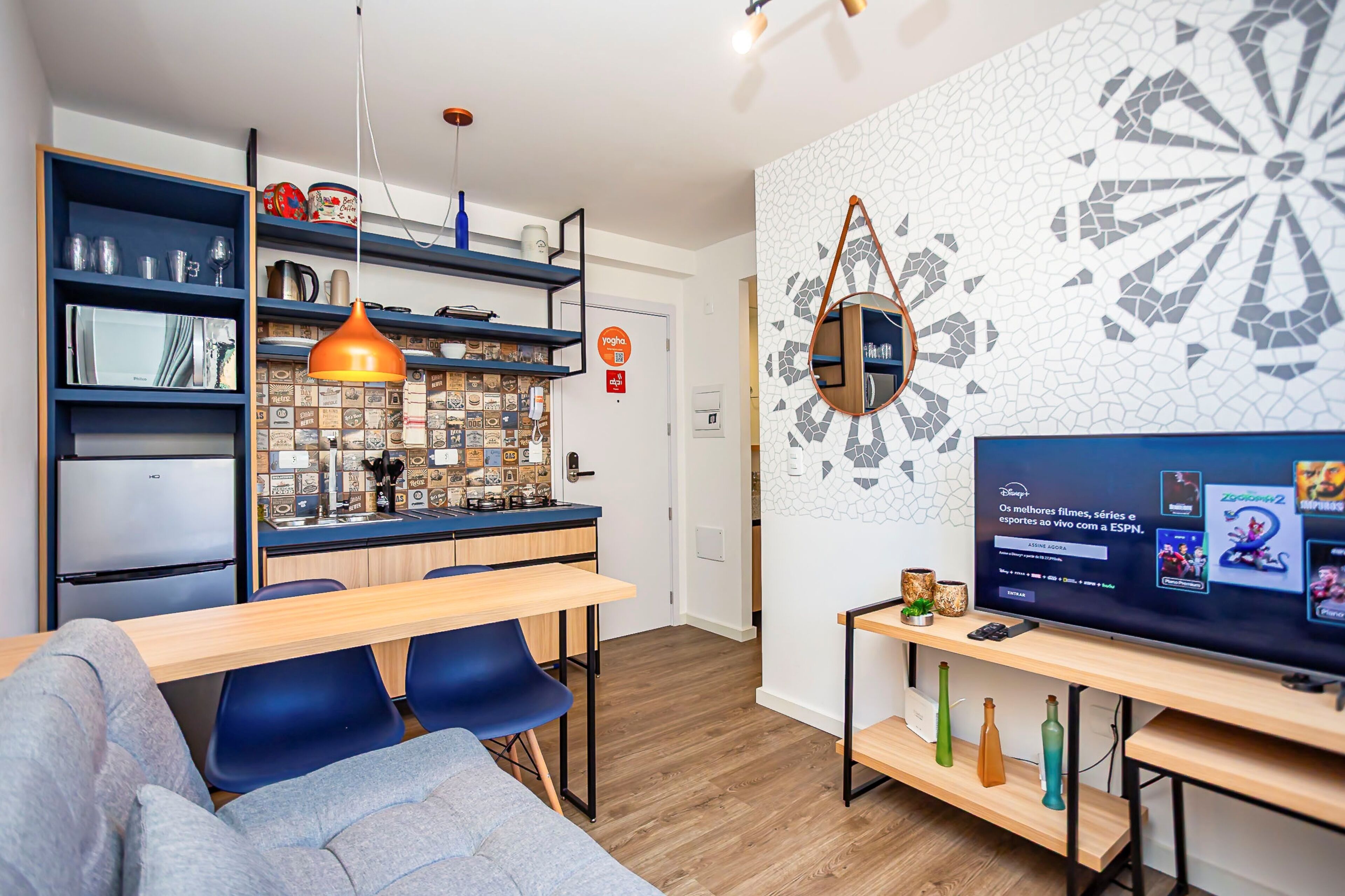 Una sala de estar moderna con un sofá, una televisión y una zona de comedor con una encimera de cocina.