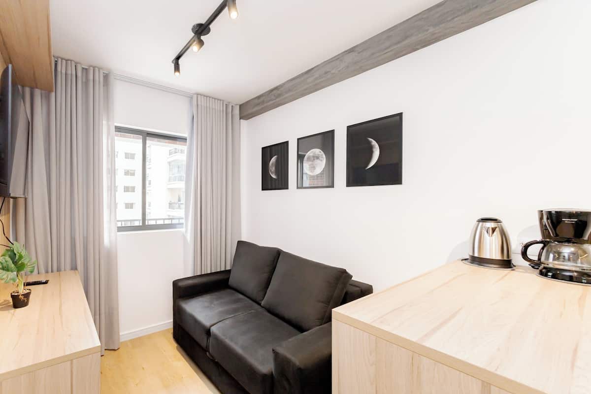 Un espace de vie moderne comprenant un canapé en cuir noir, un bureau en bois, une machine à café et des œuvres d’art encadrées accrochées au mur.