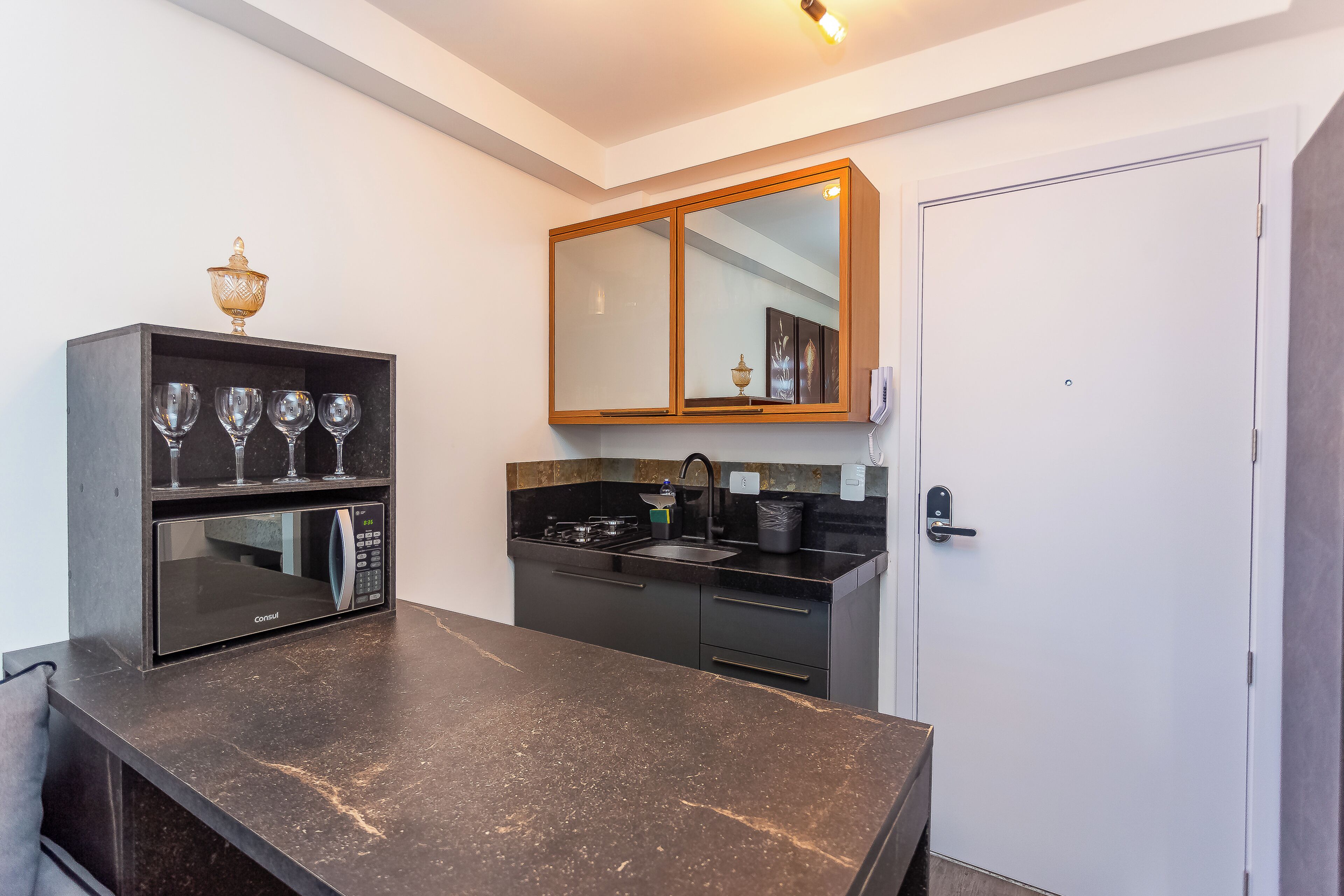 A modern kitchen with a black countertop, a microwave, a sink, and a cabinet with wine glasses.