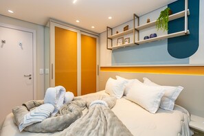 A modern hotel room with a bed, a bedside table, a wardrobe, and a shelf with decorative items.
