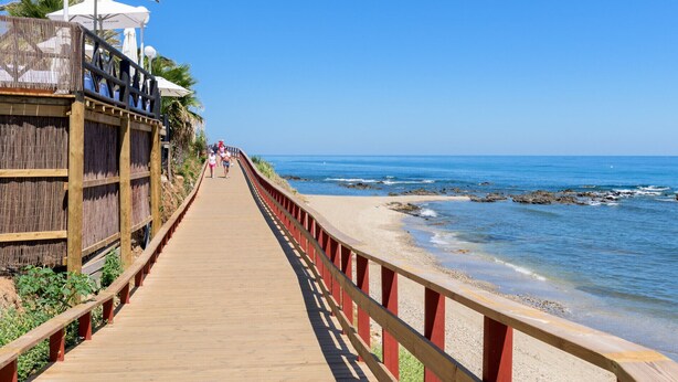 A wooden boardwalk leading to a beach with umbrellas and lounge chairs. - K13 Ocean Point - Apartment (Sitio de Calahonda)