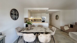 A modern dining area with a marble table, four upholstered chairs, a vase with flowers, and a wall clock. - K13 Ocean Point - Apartment (Sitio de Calahonda)