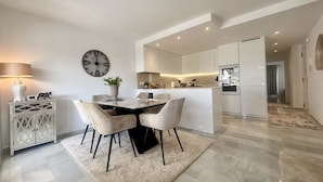 A modern kitchen with a central island, a dining area with a round table and chairs, and a living space with a sofa and a lamp. - K13 Ocean Point - Apartment (Sitio de Calahonda)