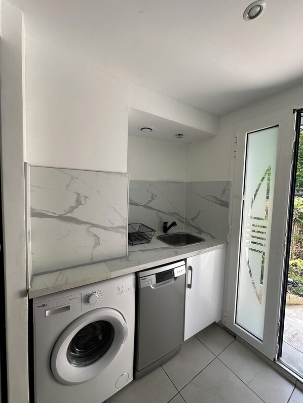 A compact kitchen with a built-in washing machine, a dishwasher, and a sink with a marble backsplash.