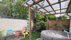 Ein Garten mit Whirlpool, einer Holz-Pergola und einem Tisch mit Stühlen.
