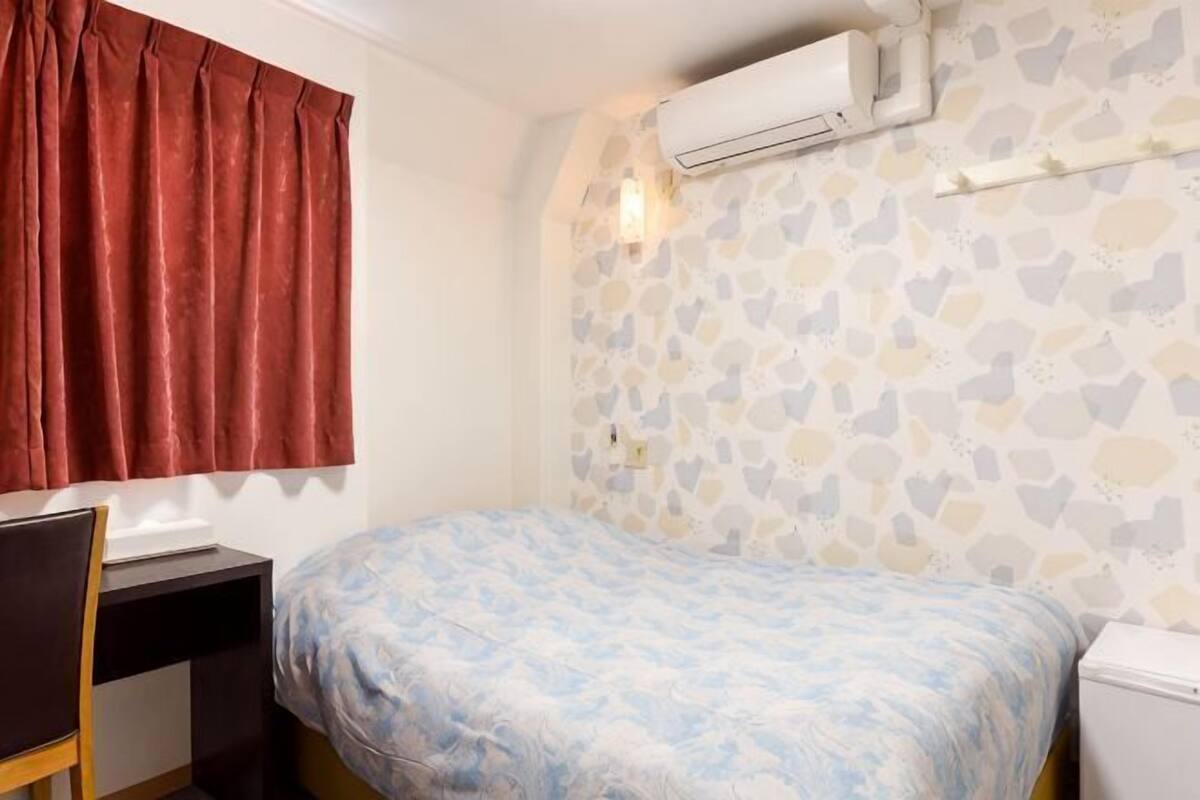A bedroom with a bed, a desk, a chair, an air conditioning unit, and a wall with a mosaic pattern.