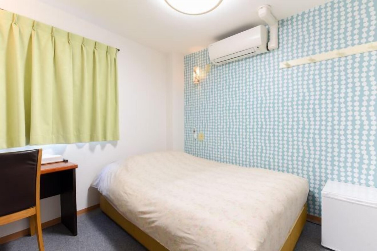 A small, single-bed room with a desk, a chair, an air conditioning unit, and a white storage unit.