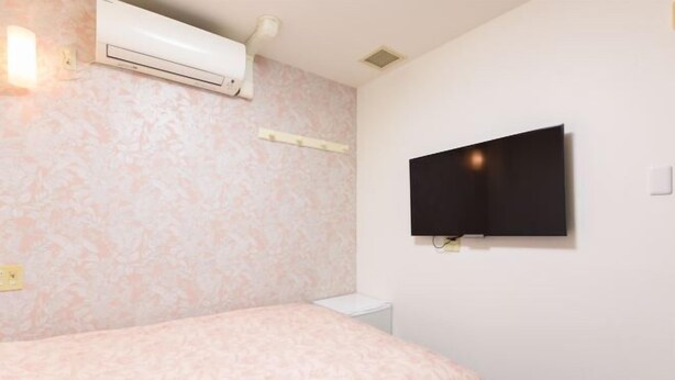 A bedroom with a bed, a wall-mounted TV, an air conditioner, and a small bedside table. - Otsuka Town Hotel (Tokyo)