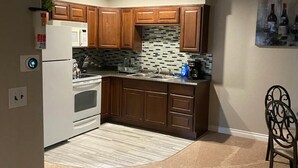 A kitchen with wooden cabinets, a white refrigerator, a tiled backsplash, and a dining area with a chair.