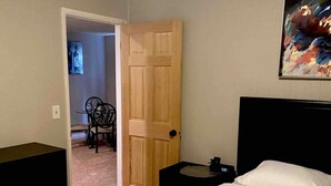 A bedroom with a bed, a wooden door, a chair, and a painting on the wall.