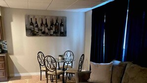 A living room with a sofa, a dining table with chairs, and a wall-mounted wine bottle display.