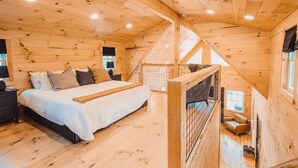 A wooden cabin bedroom with a bed, a nightstand, and a window. - Peaceful Hocking Hills Cabin | Hot Tub! Fireplace! (South Bloomingville)